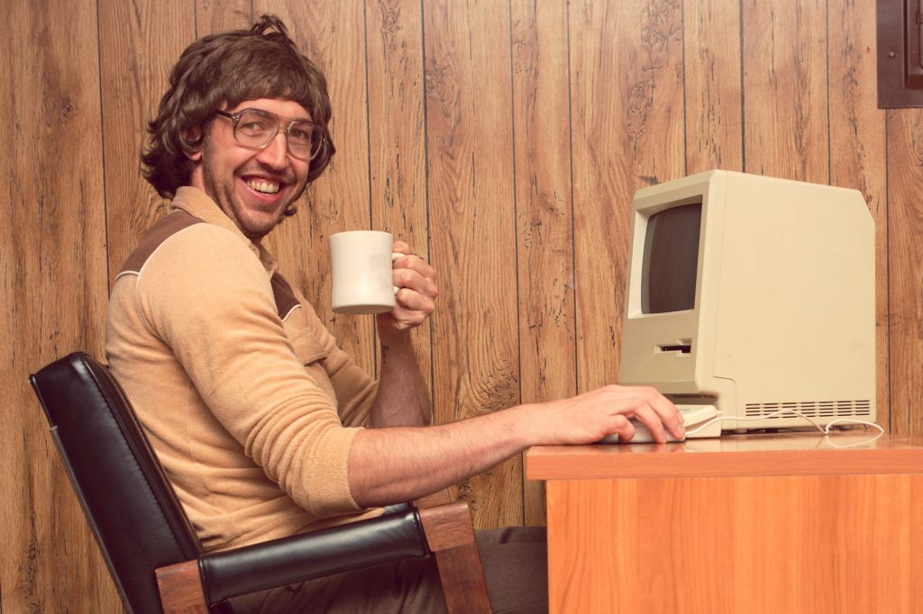 An man dressed like from the 1980s, in front of a very old personal computer.